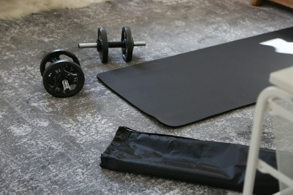 Best Compact Gym Equipment to Fit Your Small Apartment Adjustable dumbbells and an exercise mat on a floor at home