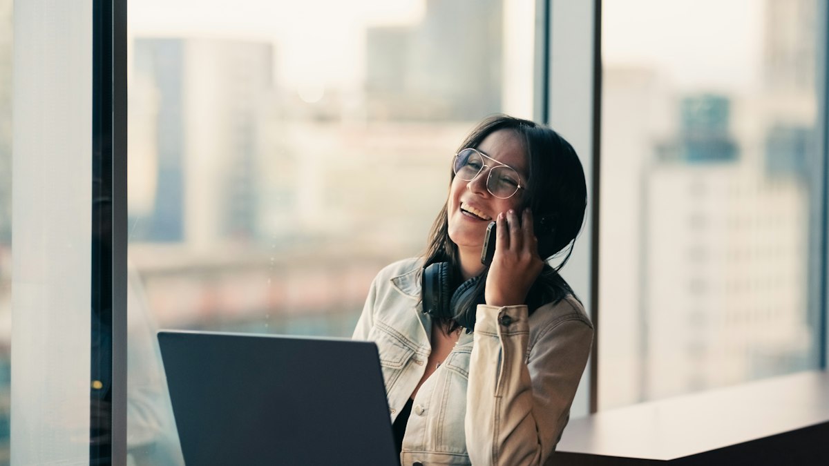 Woman laughing on a phone call by a city window