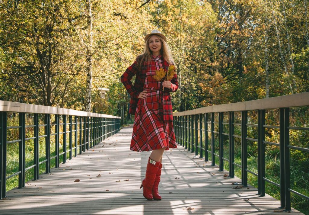 Mujer con abrigo rojo y botas sobre un puente en otoño