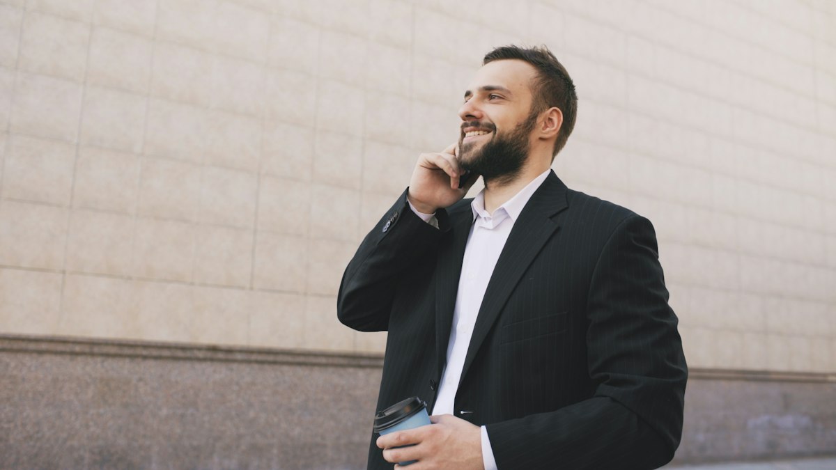 Smiling man in a suit taking a phone call outside