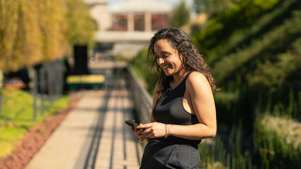 Woman smiling at her phone on a sunny walkway