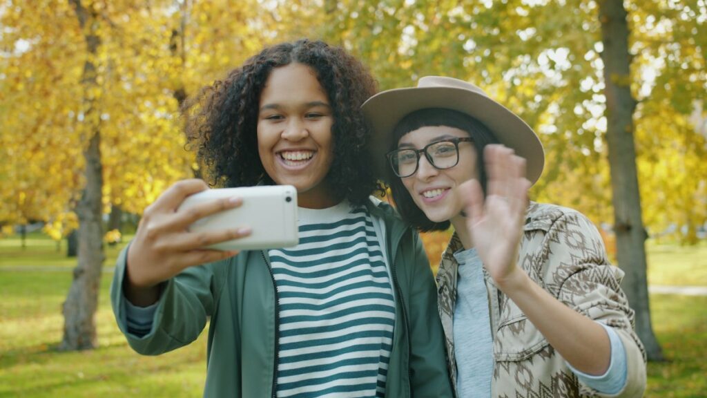 Two friends laughing on a video call outdoors in autumn