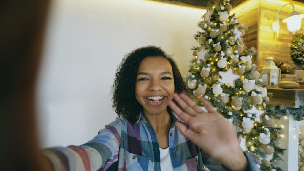Woman waving on a video call beside a Christmas tree